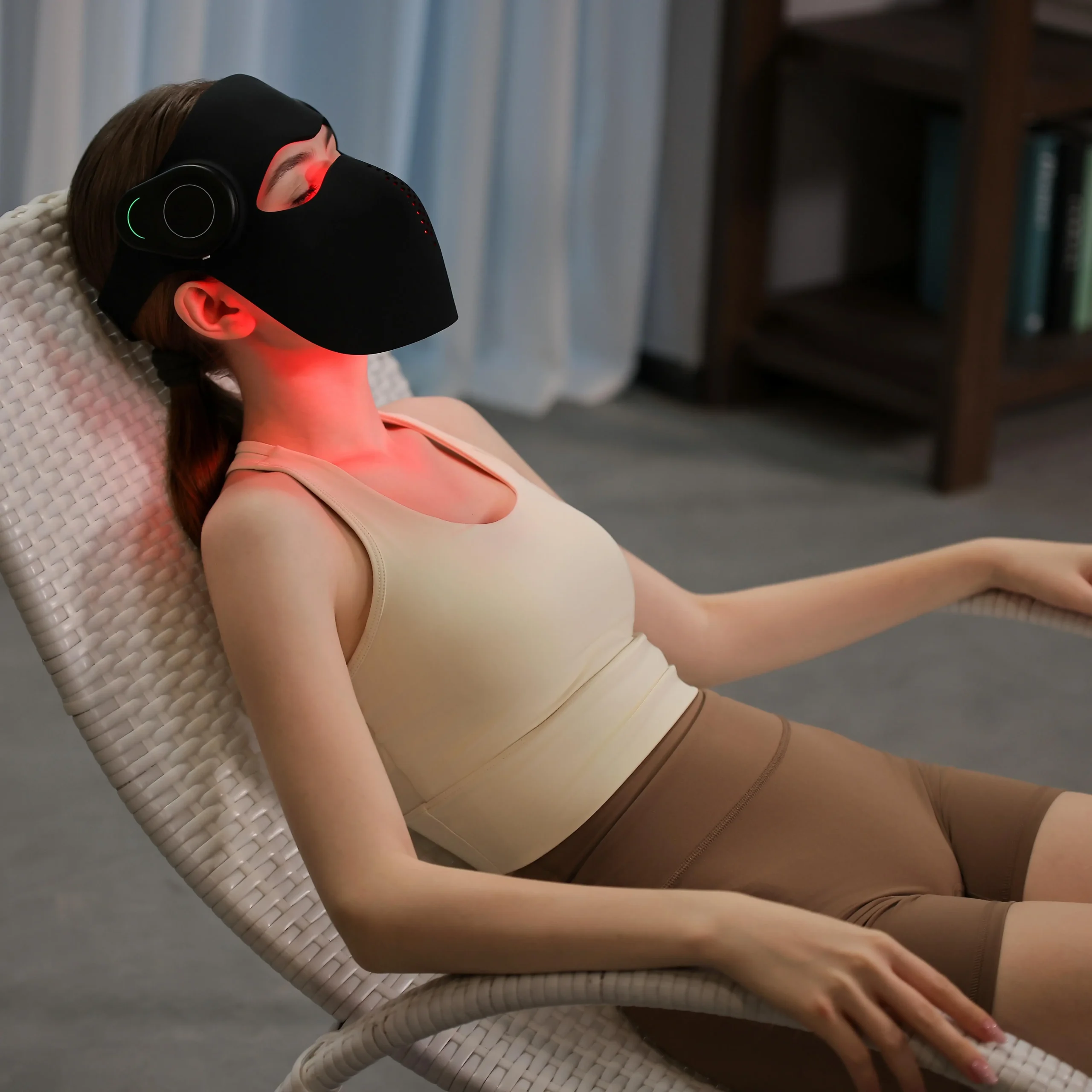 Woman relaxing in a recliner while wearing a black red light therapy face mask for face and neck